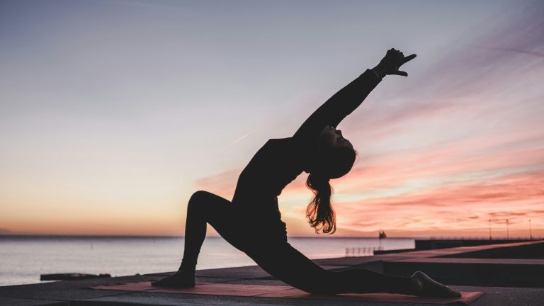 Woman doing yoga backbend on a beach at sunset