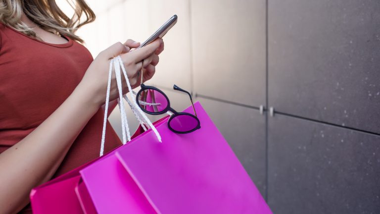Woman looking at app with shopping bags in hand