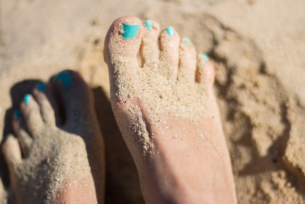 feet in the sand with blue pedicure