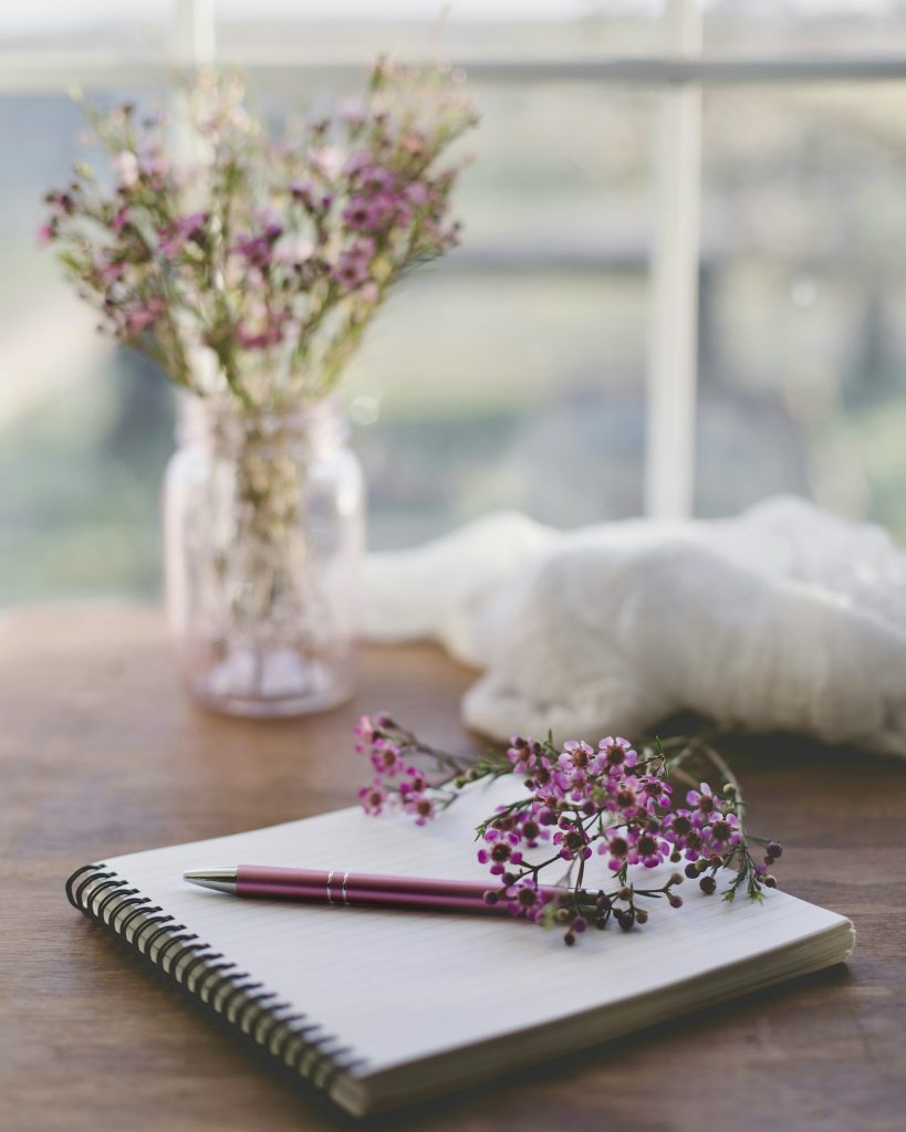 journal open at a window with fresh purple flowers in a vase