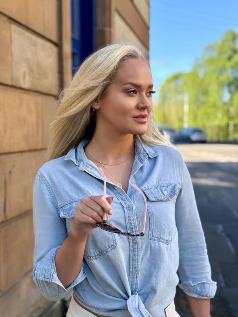 Girl in relaxed denim shirt holding Prada sunglasses 