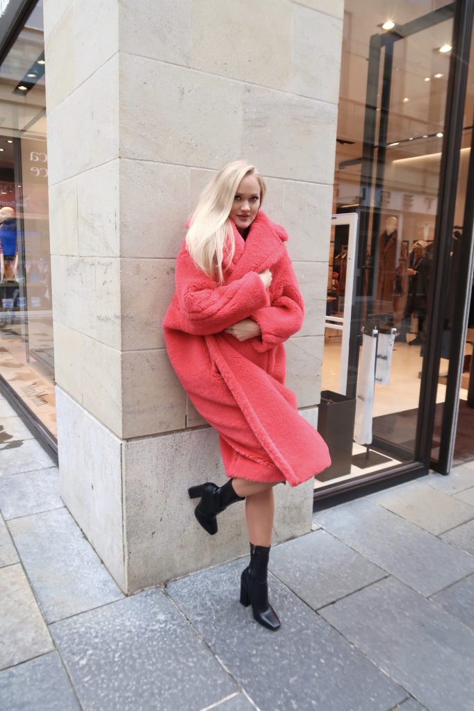 girl wears Coral red teddy coat and leans against a wall